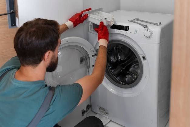 Technician in red gloves working on an open white front-loading washing machine with tools on top
