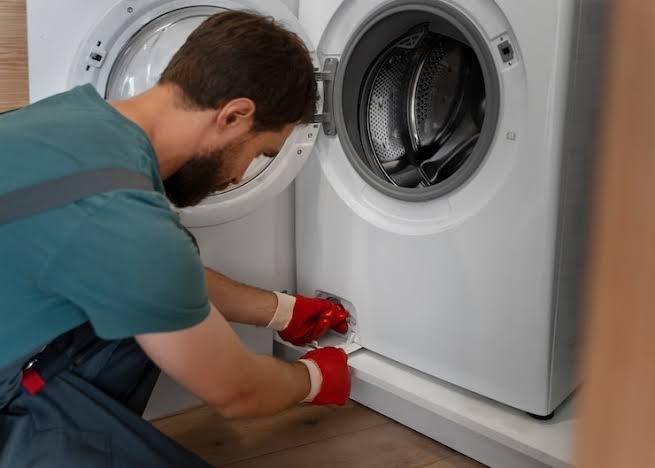 Technician in red gloves servicing two white front-loading laundry appliances
