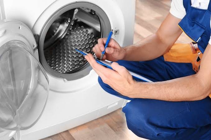 Technician inspecting an open front-loading washing machine with a clipboard and pen