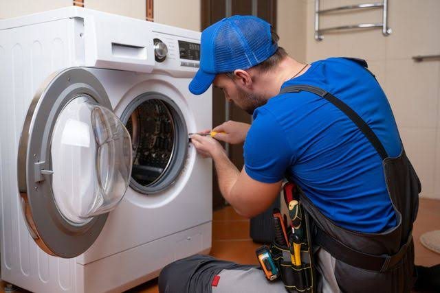 Technician in blue workwear repairing an open front-loading washing machine