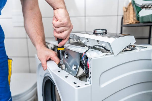 Person using a screwdriver to repair an opened front-loading washing machine with internal components exposed