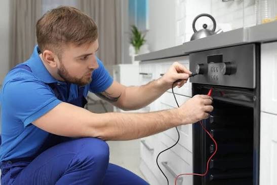 Technician using test probes on an open black oven during a repair inspection