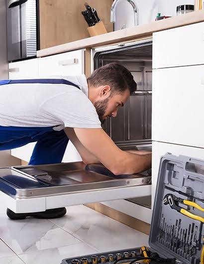 Technician in a blue apron working inside an open dishwasher in a kitchen