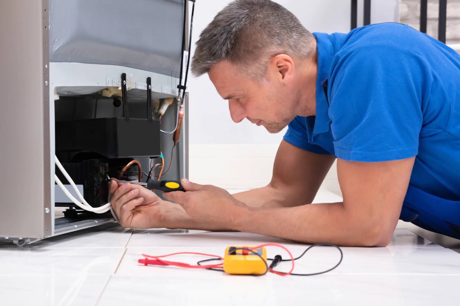 Technician inspecting exposed refrigeration components with a multimeter on the floor